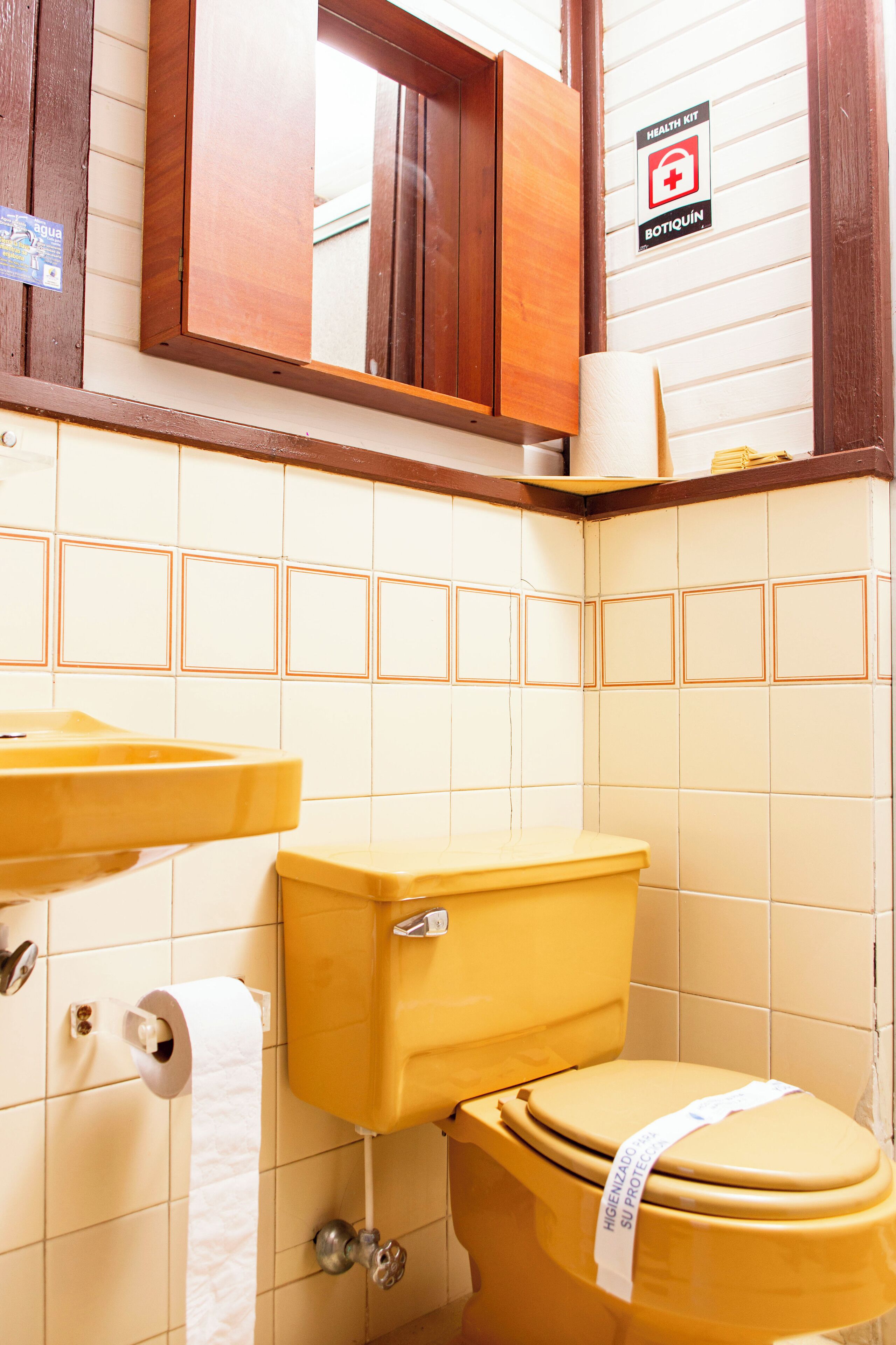 A bathroom with a yellow toilet, a sink, and a mirror above the mirror.