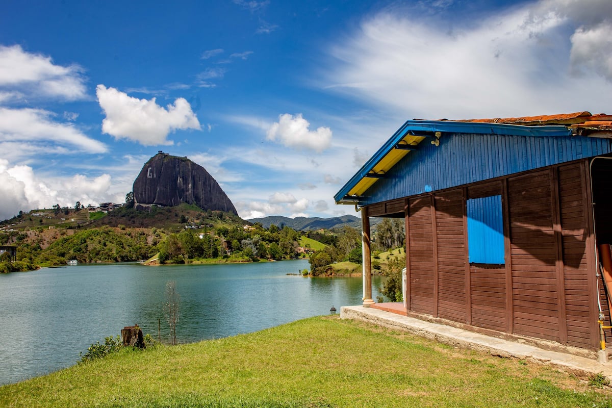 A lakeside cabin with a wooden exterior and a blue window, overlooking a calm lake and a mountain.