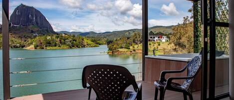 Un balcón con dos sillas que da a un lago, una montaña y una casa a lo lejos.