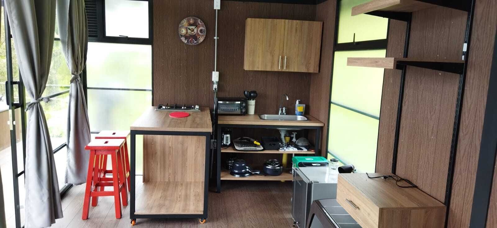 Una cocina compacta con encimera de madera, un fregadero y un pequeño comedor con un taburete rojo.