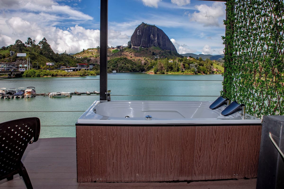 A hot tub on a wooden deck with a view of a mountain and a body of water.