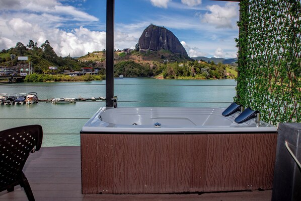 Un jacuzzi en una terraza de madera con vista a una montaña y una masa de agua.