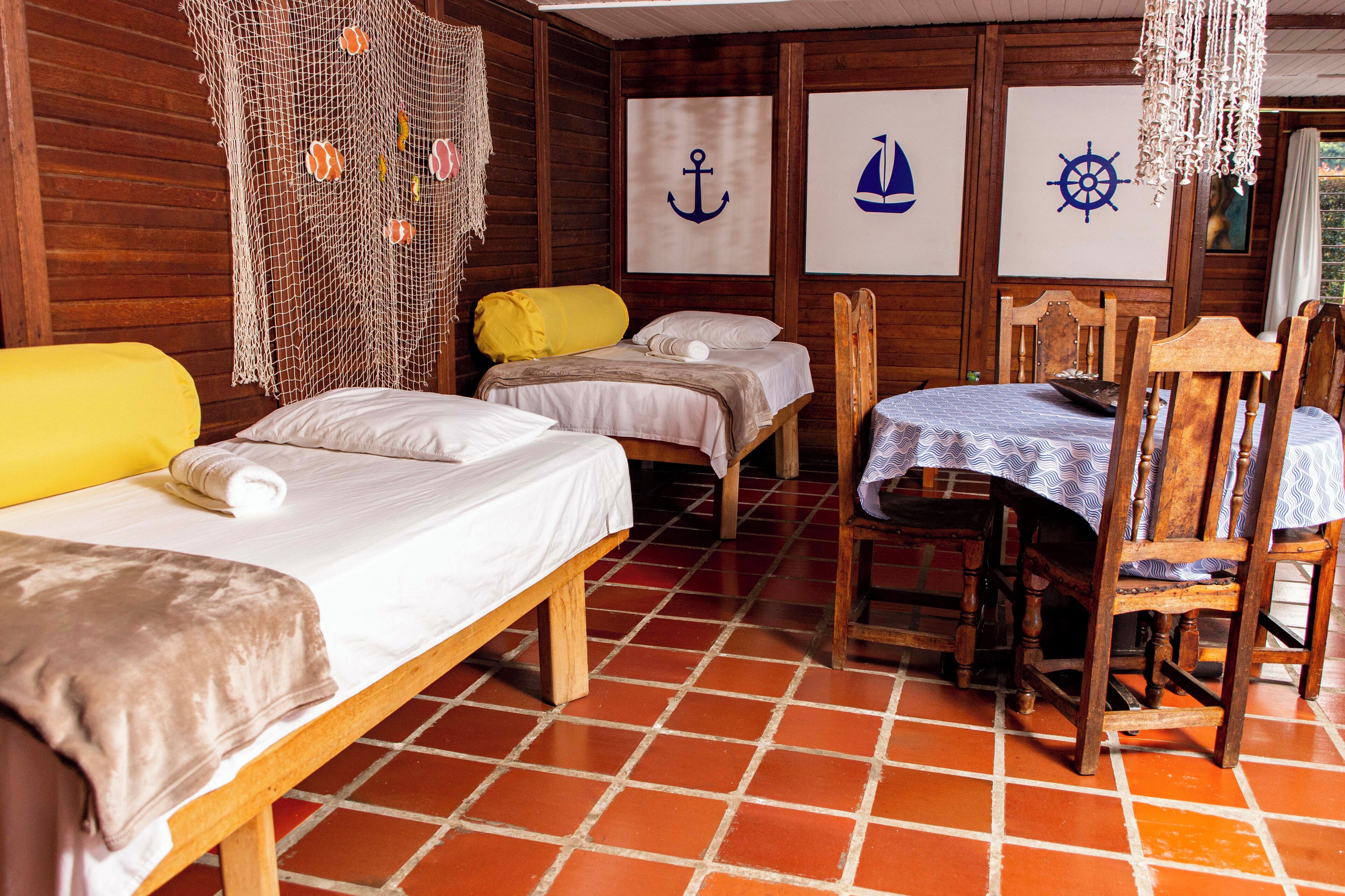 Habitación con paredes de madera, suelo de baldosas y tres camas. Decoración de temática náutica en las paredes y una mesa con sillas.