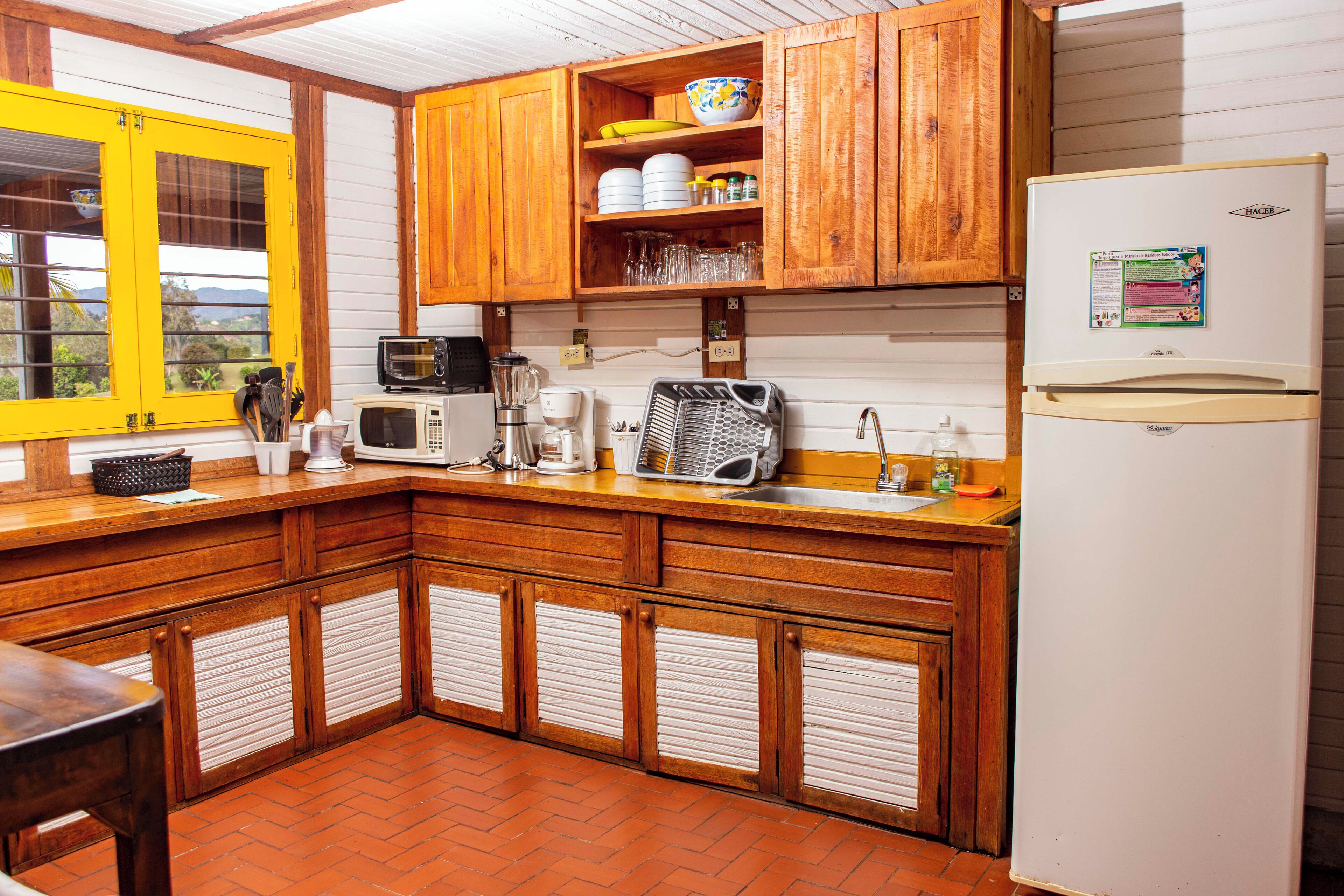 Een keuken met houten kastjes, een koelkast, een magnetron, een koffiezetapparaat en een spoelbak.