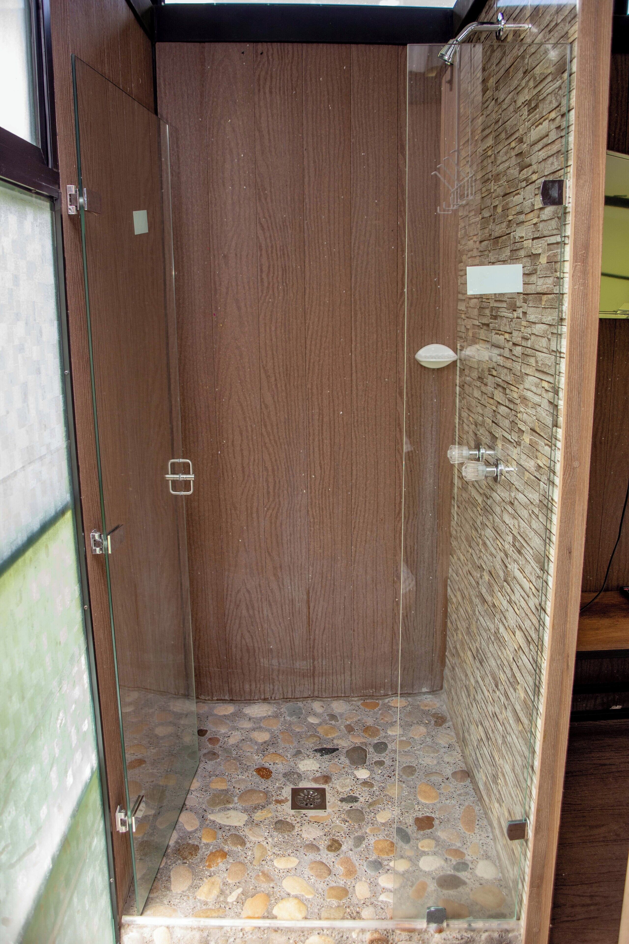 A shower with a wooden door and a pebble-patterned floor.