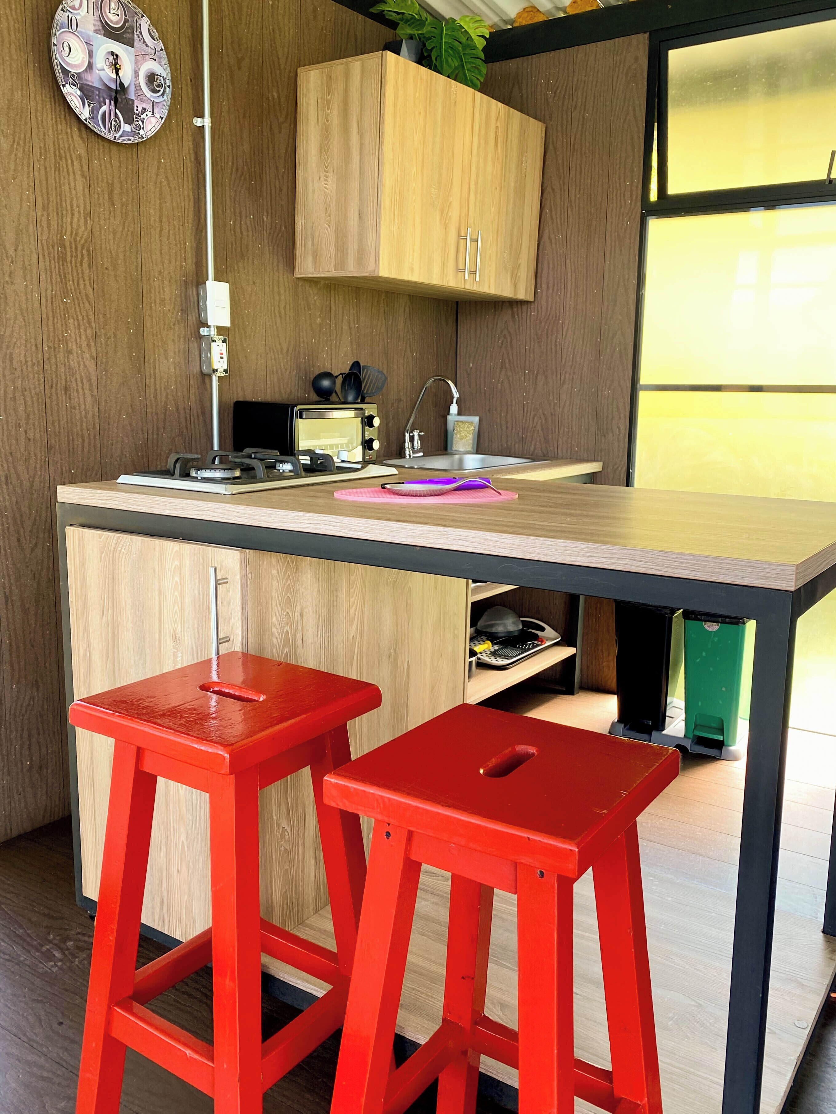 A modern kitchen with wooden cabinets, a built-in microwave, a sink, and two red stools.