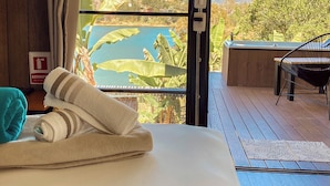 A hotel room with a large window offering a scenic view of a mountain and lake. There is a bed with neatly folded towels and a chair outside the window. - Cabañas Navegar (El Peñol)