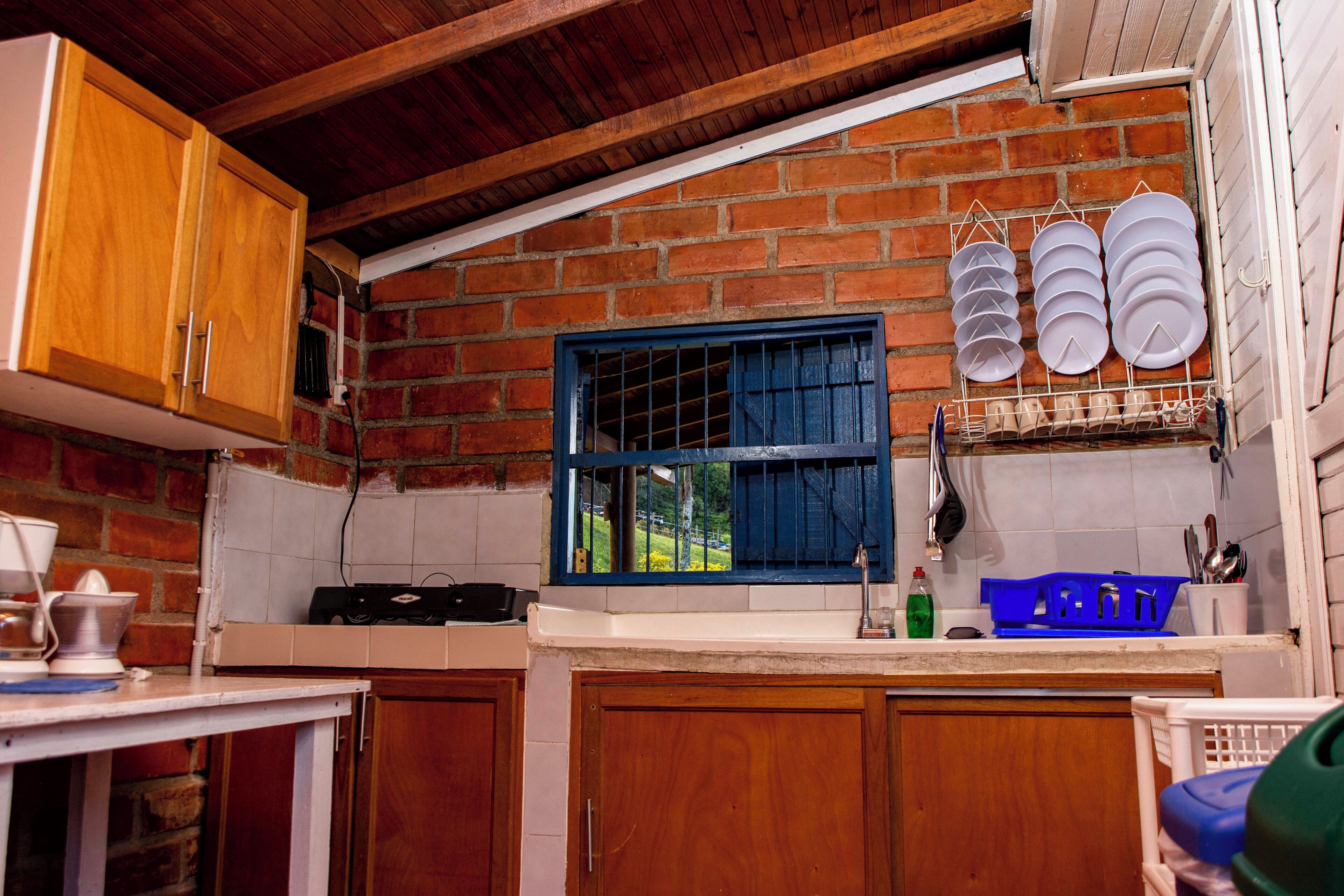 A kitchen with wooden cabinets, a brick wall, a window with blue shutters, and a dish rack with plates.