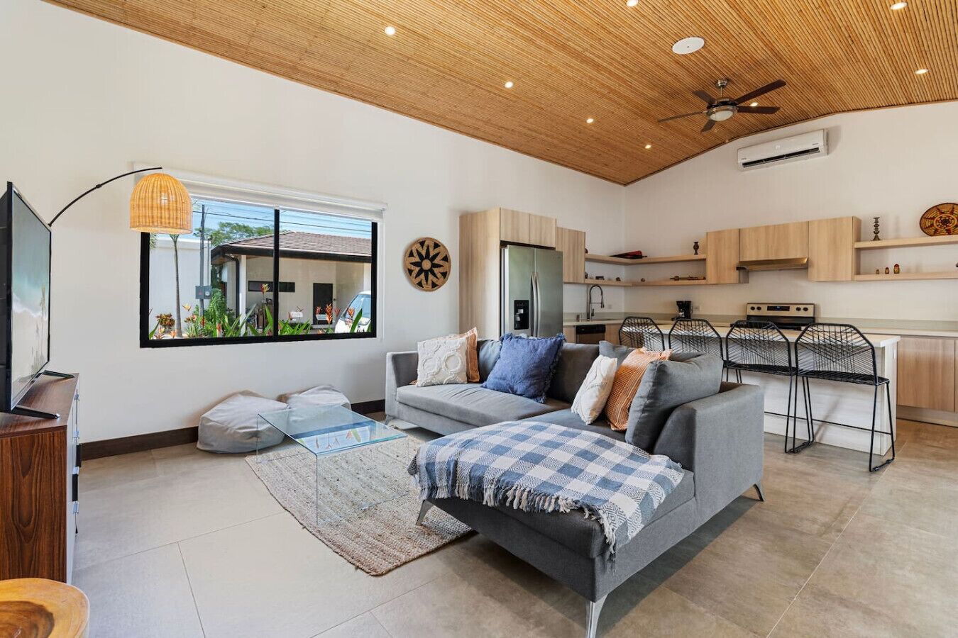 A modern living room with a grey sofa, a glass coffee table, and a wooden ceiling.