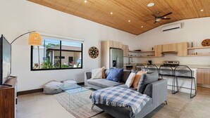 A modern living room with a grey sofa, a glass coffee table, and a wooden ceiling.