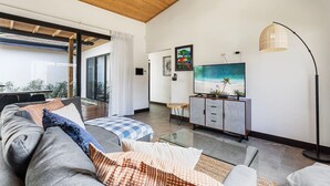 A modern living room with a large flat-screen TV, a glass coffee table, and a sofa with patterned cushions.