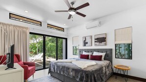 A modern bedroom with a large bed, a ceiling fan, and a view of the outdoors.