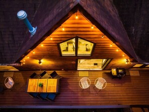 Une charmante cabane en bois, dotée d’un toit en pente, d’une lucarne centrale et d’un petit balcon avec des sièges.