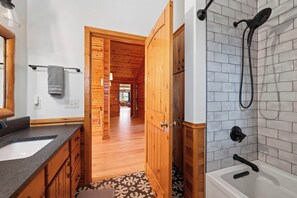 A bathroom with a wooden vanity, a shower, and a hallway leading to a living area.