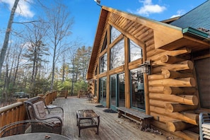 A log cabin with a deck, large windows, and outdoor furniture. - Dog Friendly Cabin - sleeps 12 (Fish Creek)