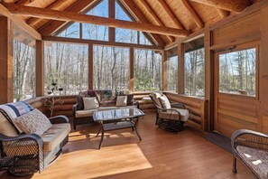 A log cabin with a wooden interior, large windows, a glass coffee table, wicker furniture, and a view of the forest.