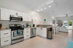 A modern kitchen with white cabinetry, stainless steel appliances, and a dining area with a white table and chairs.