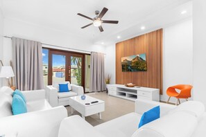 A modern living room with white furniture, a ceiling fan, and a large window with curtains.