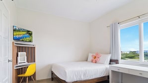 Une chambre à coucher avec un lit, un bureau, une chaise, un téléviseur et une fenêtre donnant sur un beau paysage.