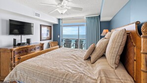 A bedroom with a large bed, a ceiling fan, a TV, a dresser, and a view of the ocean. - Crescent Keyes 904 - 3BD/3BA Oceanfront Condo (North Myrtle Beach)