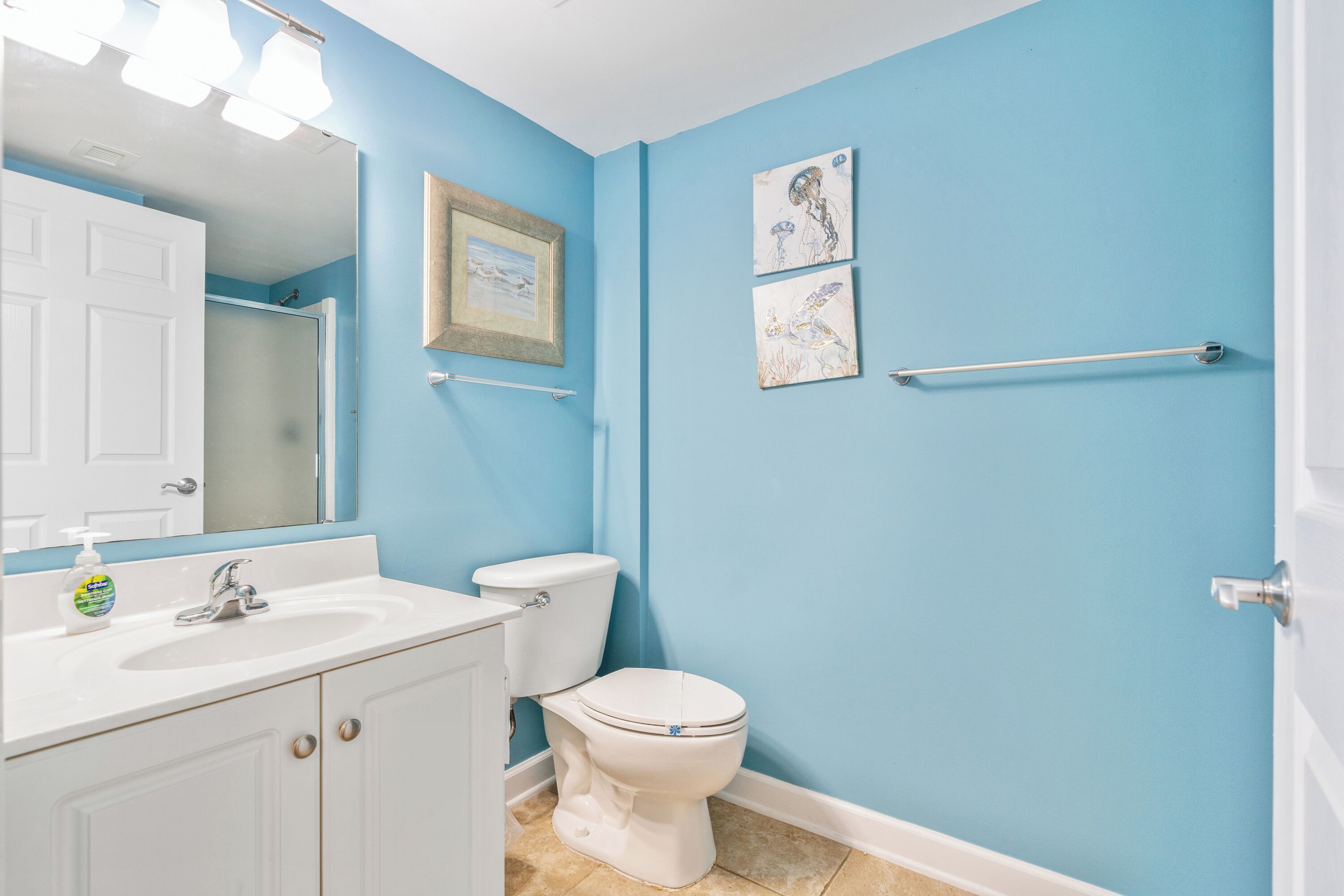 A bathroom with a white sink, a white toilet, and a blue wall. There is a framed picture on the wall and a towel rack.