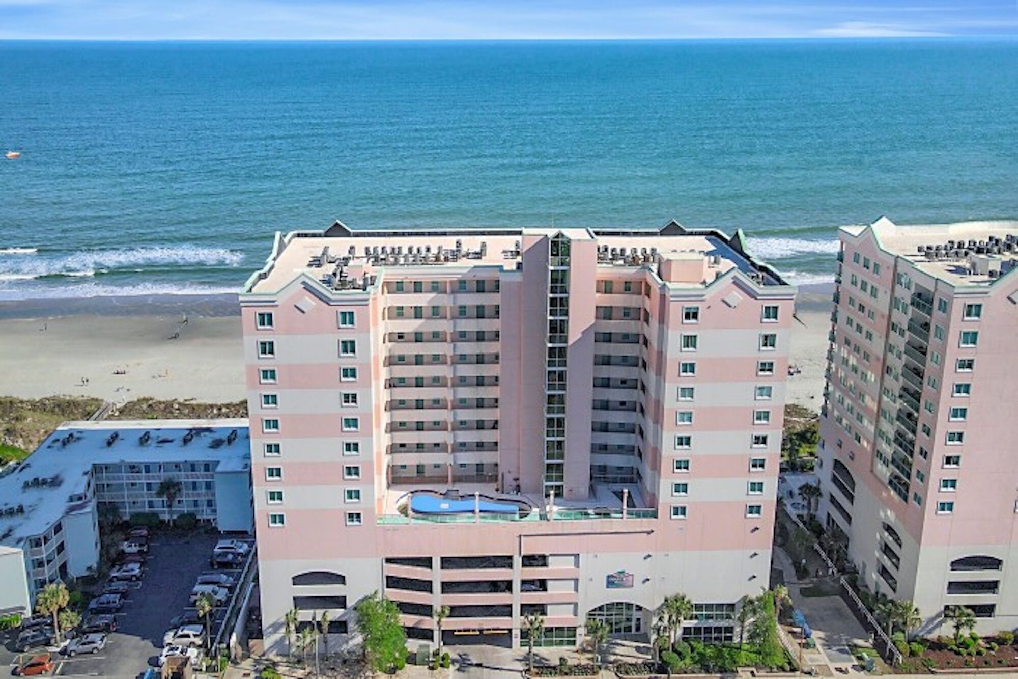 A multi-story hotel with a rooftop pool, located near a beach with ocean views.