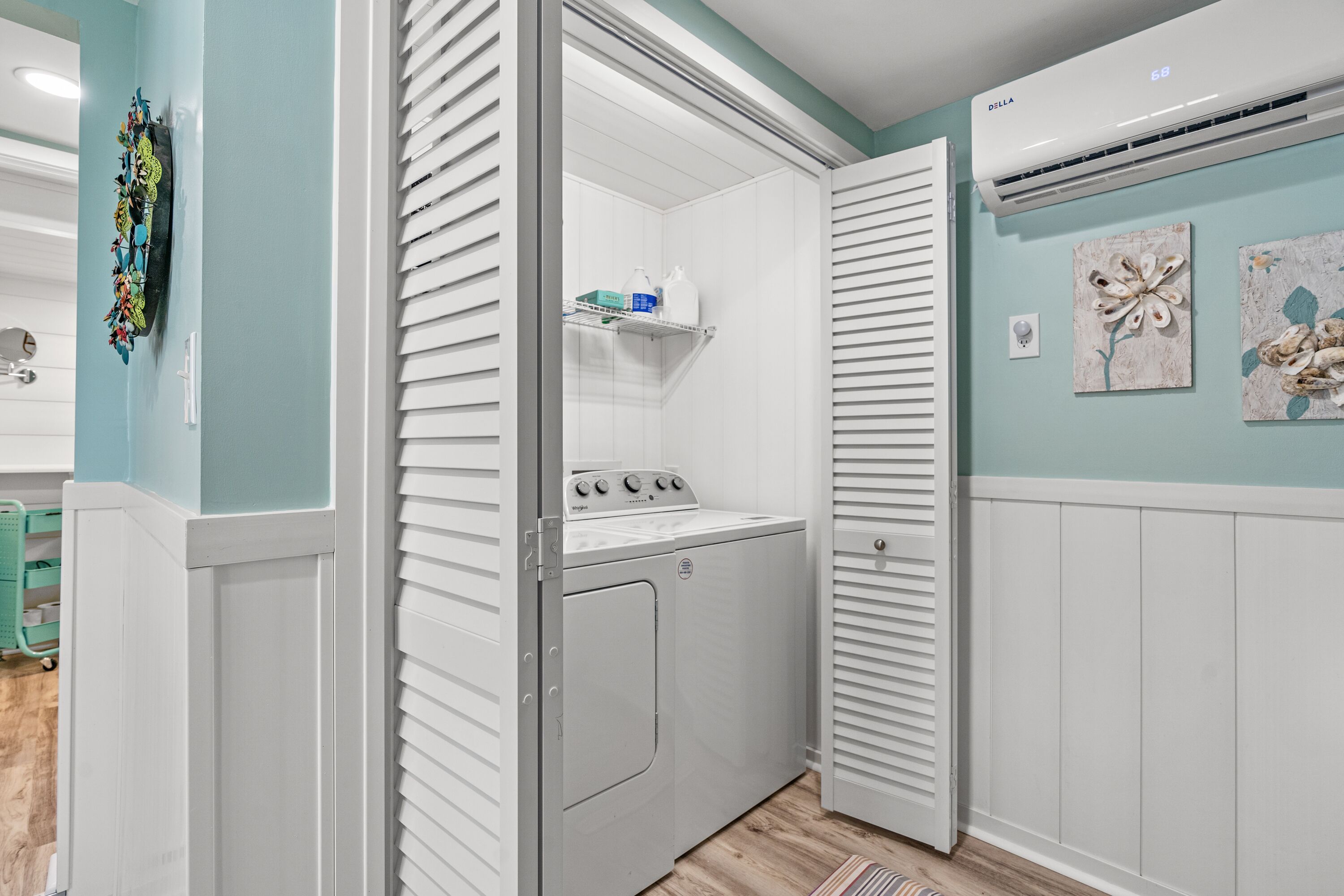 A laundry room with a washing machine, a shelf with cleaning supplies, and a wall-mounted air conditioner.