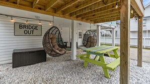 A covered outdoor seating area with wicker chairs, a picnic table, and a 'Bridge Out' sign. - Pet Friendly 3 BR House - Latitude Adjustment (North Myrtle Beach)
