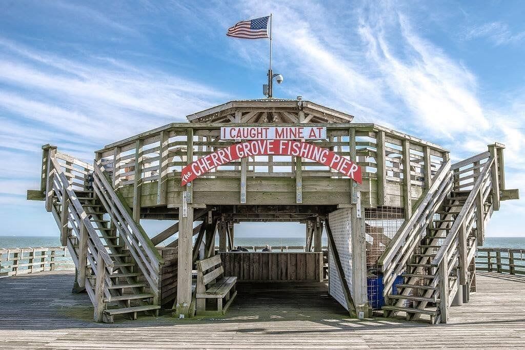Een houten pier met een bord waarop staat: 'Ik heb de mijne gevangen bij Cherry Grove Fishing Pier'.