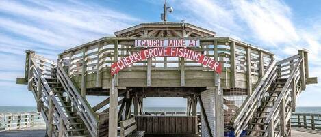 A wooden pier structure with a sign that reads "I Caught Mine at Cherry Grove Fishing Pier."