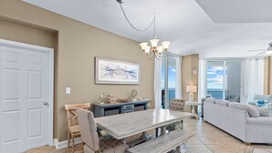 A spacious living area with a dining table, bench, and a large window offering a view of the outdoors. - Lighthouse 1004 (Gulf Shores)