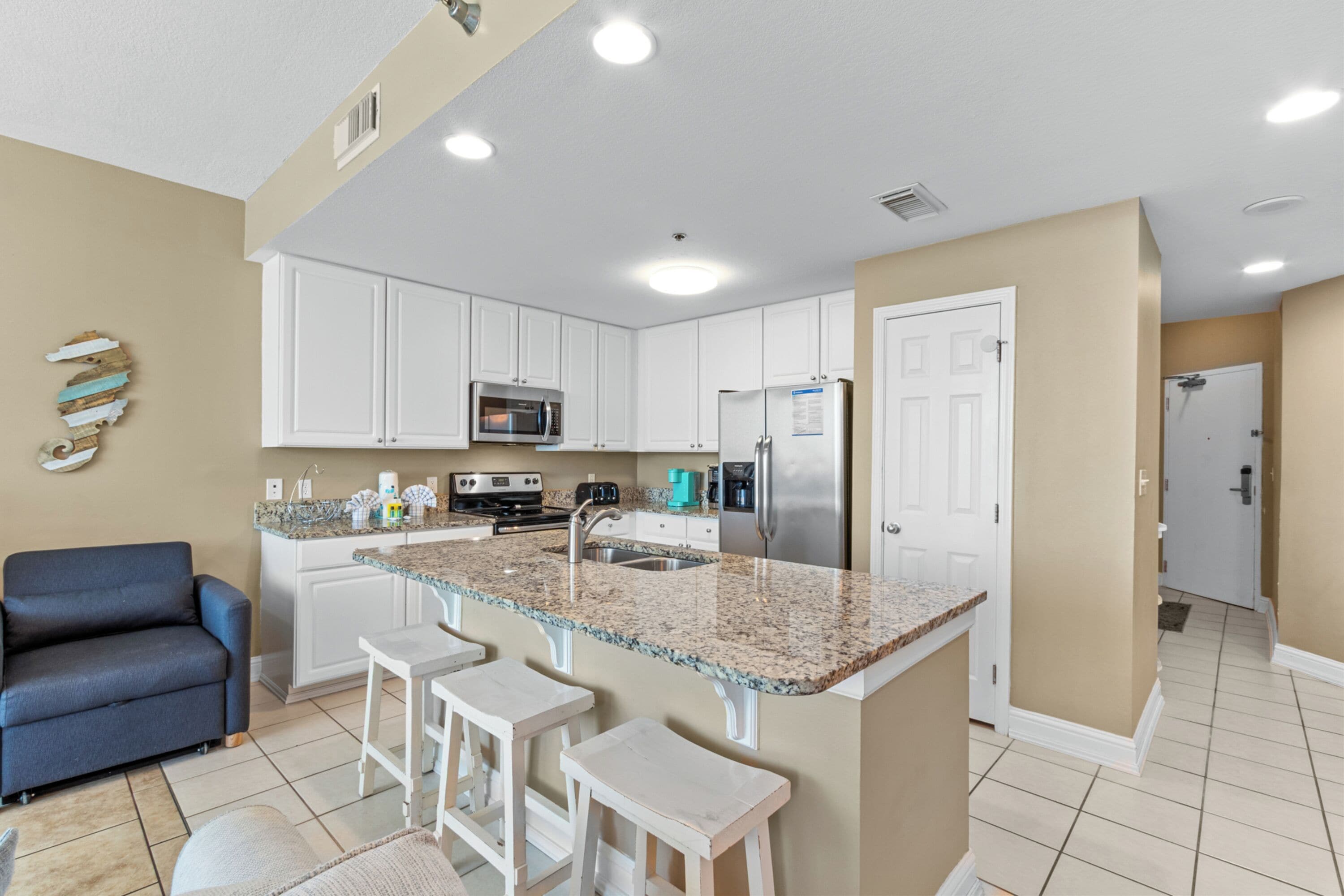 A modern kitchen with white cabinets, granite countertops, a built-in microwave, and a stainless steel refrigerator.