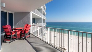 A balcony with a table and chairs, overlooking a beach with people and a clear sky. - Lighthouse 1004 (Gulf Shores)