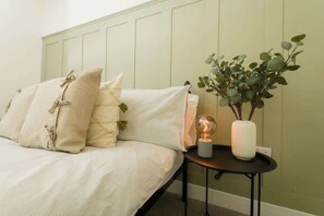A bed with pillows, a bedside table with a lamp, and a plant.