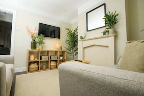 A living room with a sofa, a TV mounted on the wall, a fireplace, and a bookshelf with decorative items.