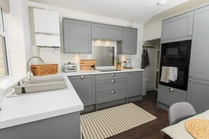 A compact kitchen with grey cabinets, a white countertop, a built-in oven, and a small dining area.