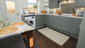 A compact kitchen with grey cabinets, a washing machine, a dining table with placemats, and a view of the outside. - Close to Castle | Free Wi-Fi | Close to Cathedral (Lincoln)