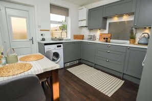 A compact kitchen with grey cabinets, a washing machine, a dining table with placemats, and a view of the outside.