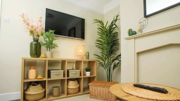 A living room with a TV, shelves with decorative items, a large plant, and a round table with a remote. - Close to Castle | Free Wi-Fi | Close to Cathedral (Lincoln)