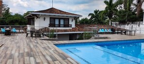 A house with a swimming pool, a patio with chairs, and a view of the surrounding area.