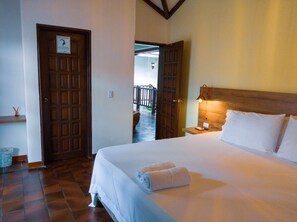 A hotel room with a large bed, a wooden headboard, a nightstand, and a door leading to a balcony.