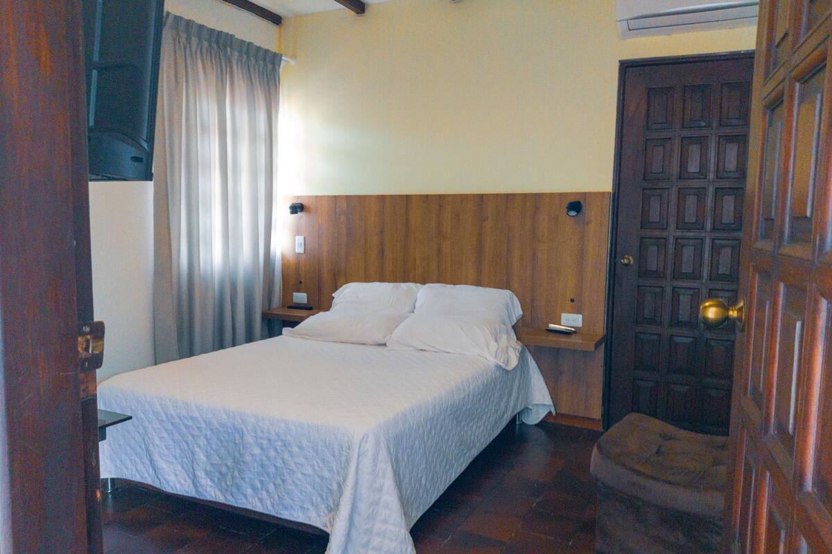 Camera da letto con un letto, testiera in legno, comodini, una porta e una finestra con tende.