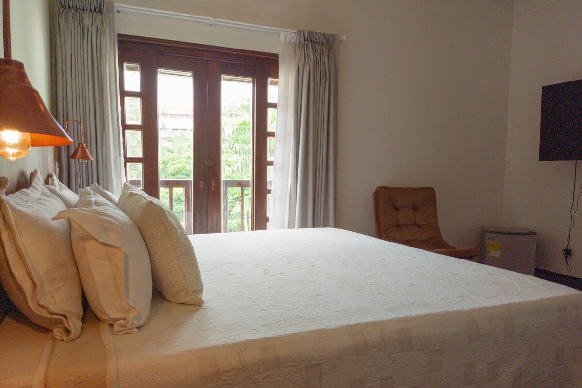 Una camera da letto con un letto grande, una sedia, una televisione e una finestra con tende.