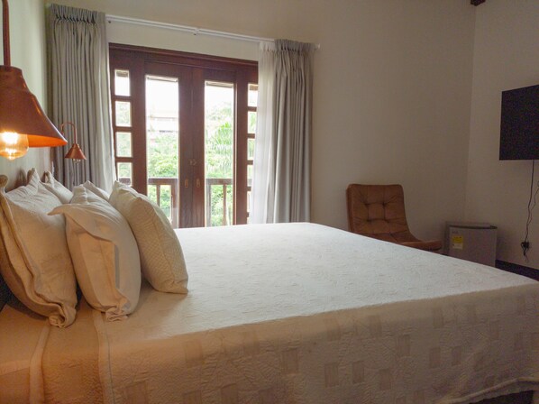 Un dormitorio con una cama grande, una silla, un televisor y una ventana con cortinas.