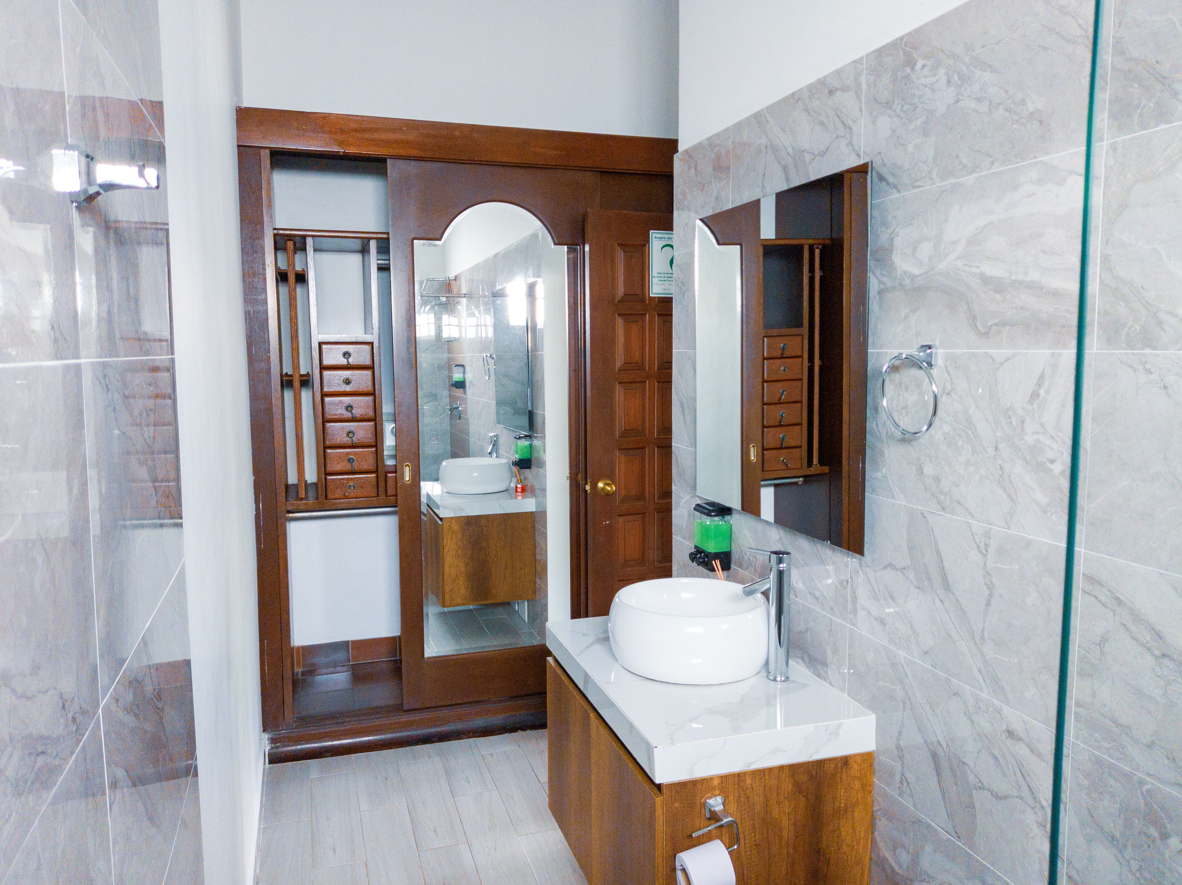 A modern bathroom with a wooden vanity, a large mirror, and a marble-tiled wall.