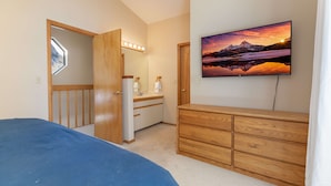 A bedroom with a bed, a dresser, a vanity with a mirror, and a TV on the wall.