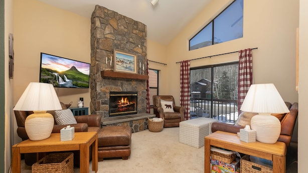 A cozy living room with a stone fireplace, leather furniture, and a large window with curtains.