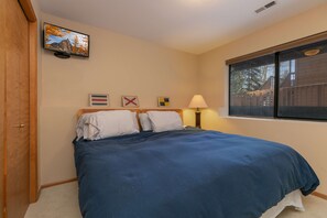 Un dormitorio con cama, televisión montada en la pared, ventana con vista a una valla de madera y una puerta.