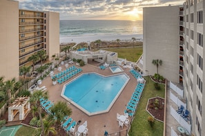 A hotel with a pool surrounded by lounge chairs and a view of the ocean.