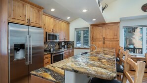 Cocina con armarios de madera, electrodomésticos de acero inoxidable, encimera de granito y comedor con sillas de madera.